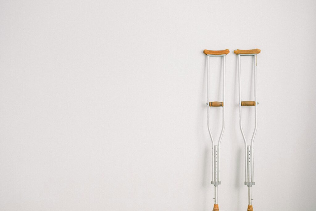 Minimalist image of a pair of crutches leaning on a white wall, symbolizing mobility aid.