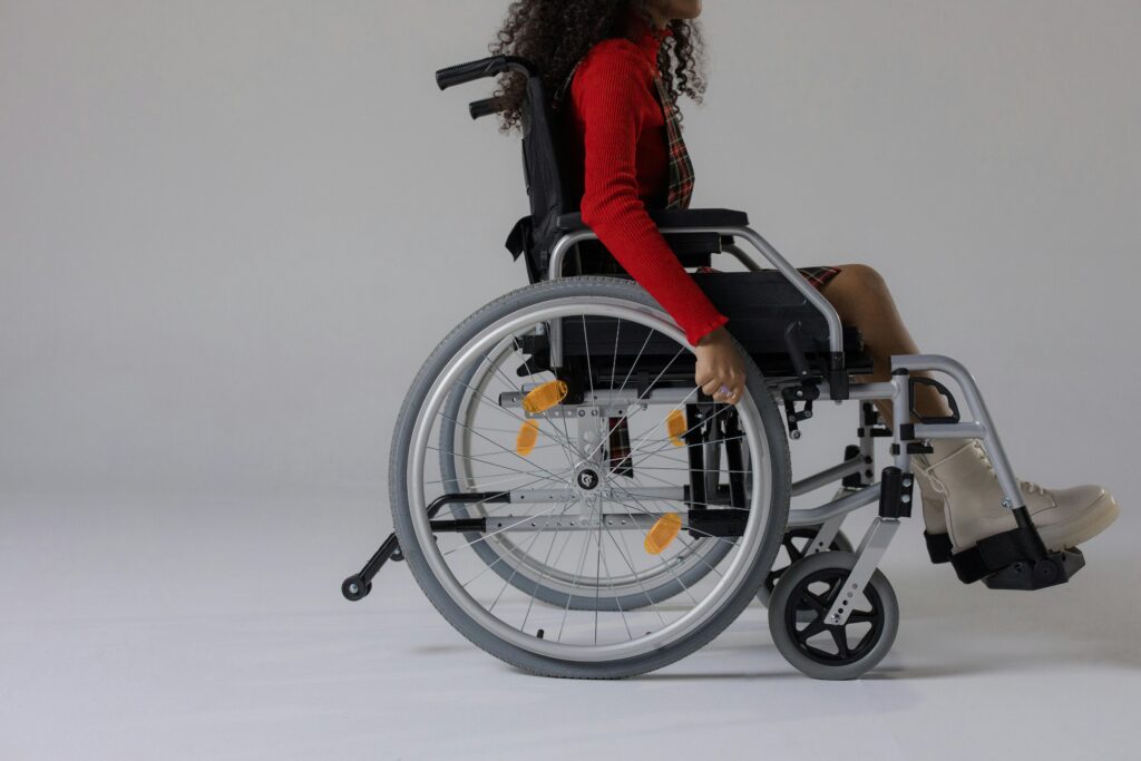 Studio shot of a young woman with curly hair in a wheelchair against a gray background.